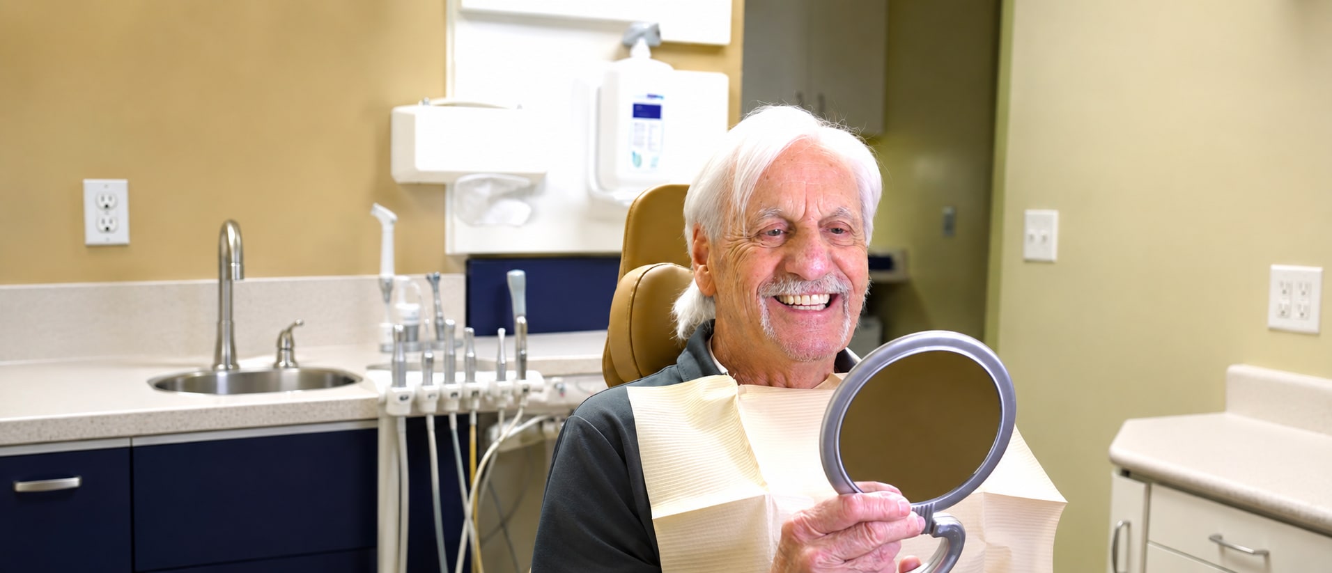 A patient at the St. George Center for Specialized Dentistry smiling in the chair, holding a hand mirror to see his new smile.